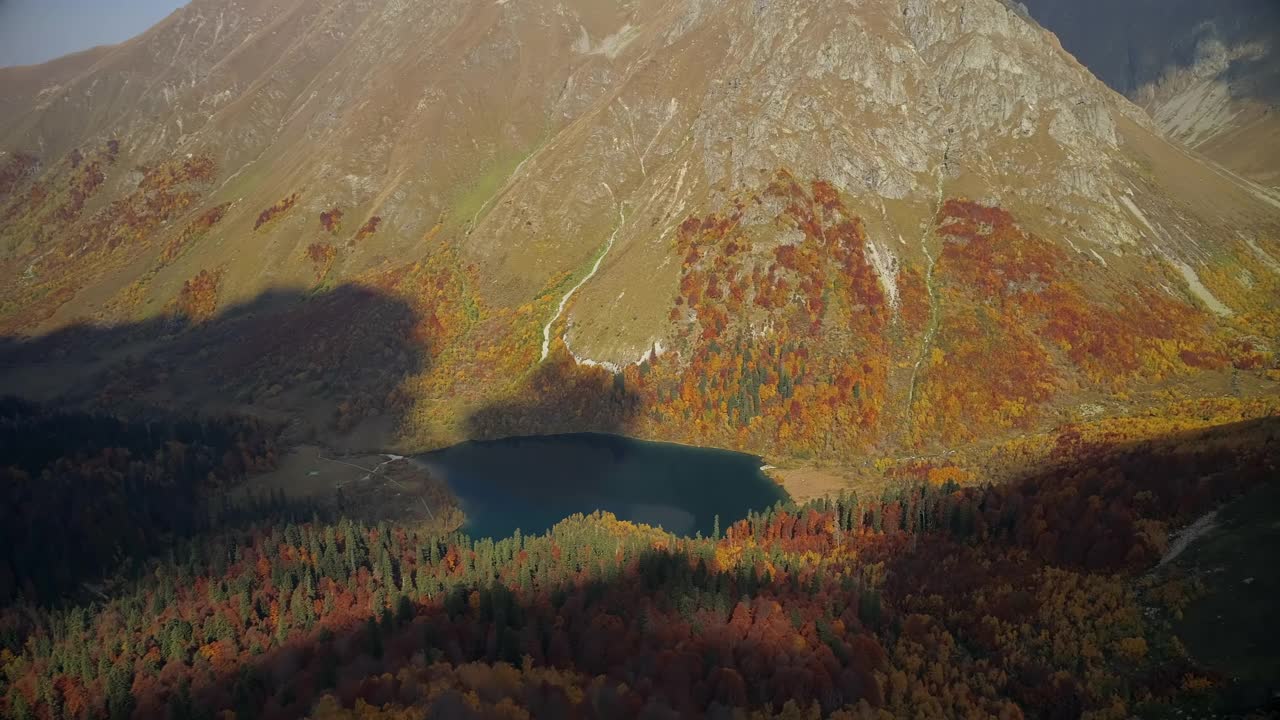 山谷中有一个清澈的高山湖泊，周围是秋天的森林。山谷中橙色、红色和黄色的森林。雄蜂飞过五彩缤纷的森林。非常美丽的山脉全景鸟瞰图视频素材