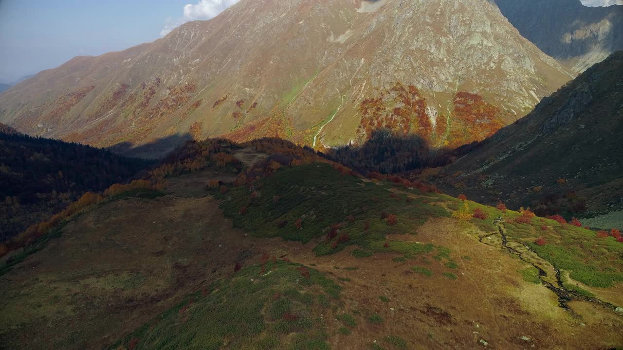 山谷中有一个清澈的高山湖泊，周围是秋天的森林。山谷中橙色、红色和黄色的森林。雄蜂飞过五彩缤纷的森林。非常美丽的山脉全景鸟瞰图视频素材