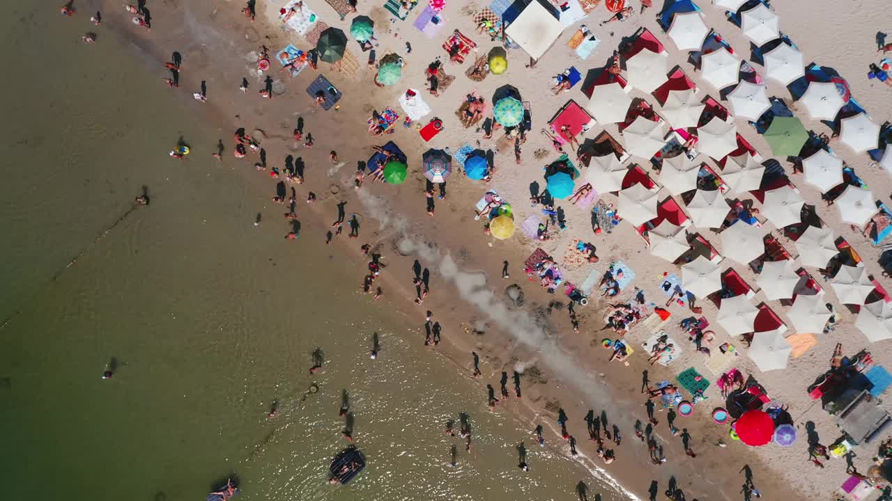 在炎热的夏天鸟瞰城市海滩。白色的沙滩上放着遮阳伞。视频素材