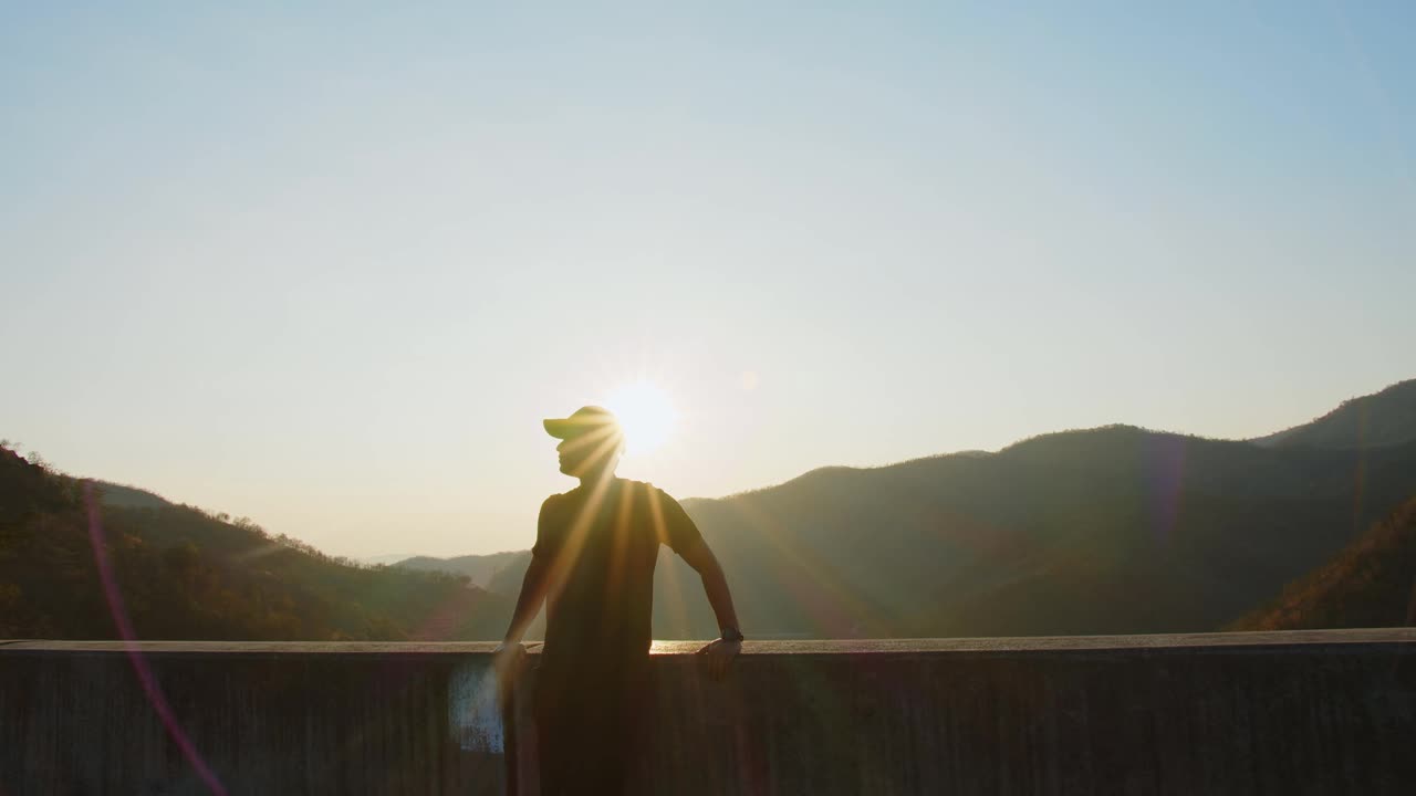 剪影嬉皮士徒步旅行者英俊的男人站在山上，看着美丽的大自然，看着夕阳西下的阳光视频素材