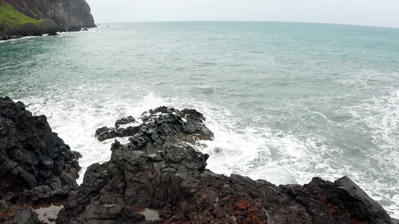 4K滑块海浪挤压黑色岩石在海岸泡沫视频素材