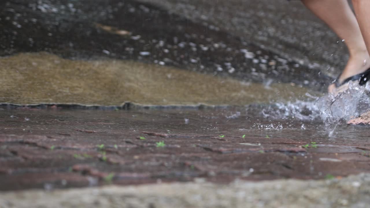 低角度拍摄脚穿人字拖在大雨倾盆的日子里奔跑，被洪水淹没的街道，暴风台风季风季节里奔跑，湿脚在水坑里奔跑，湿鞋在雨天湿透视频素材