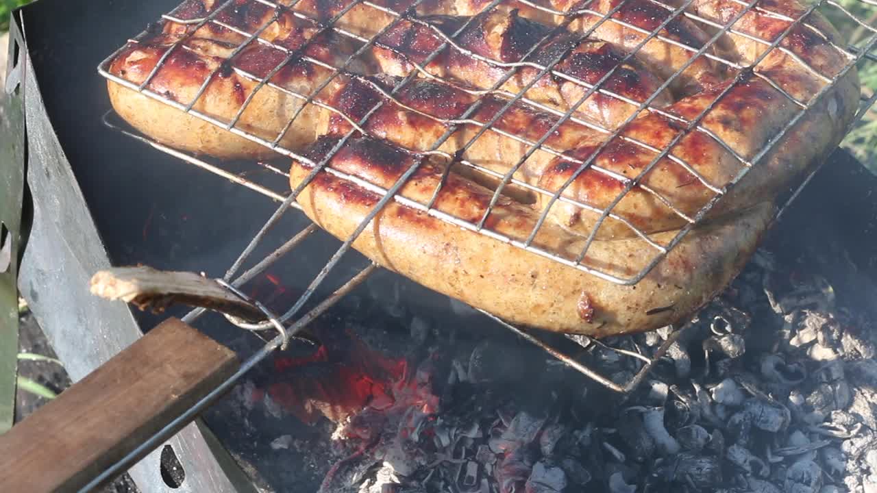 烤架烤香肠。在木炭烤架上。在绿草如茵的草地上野餐。特写镜头视频素材