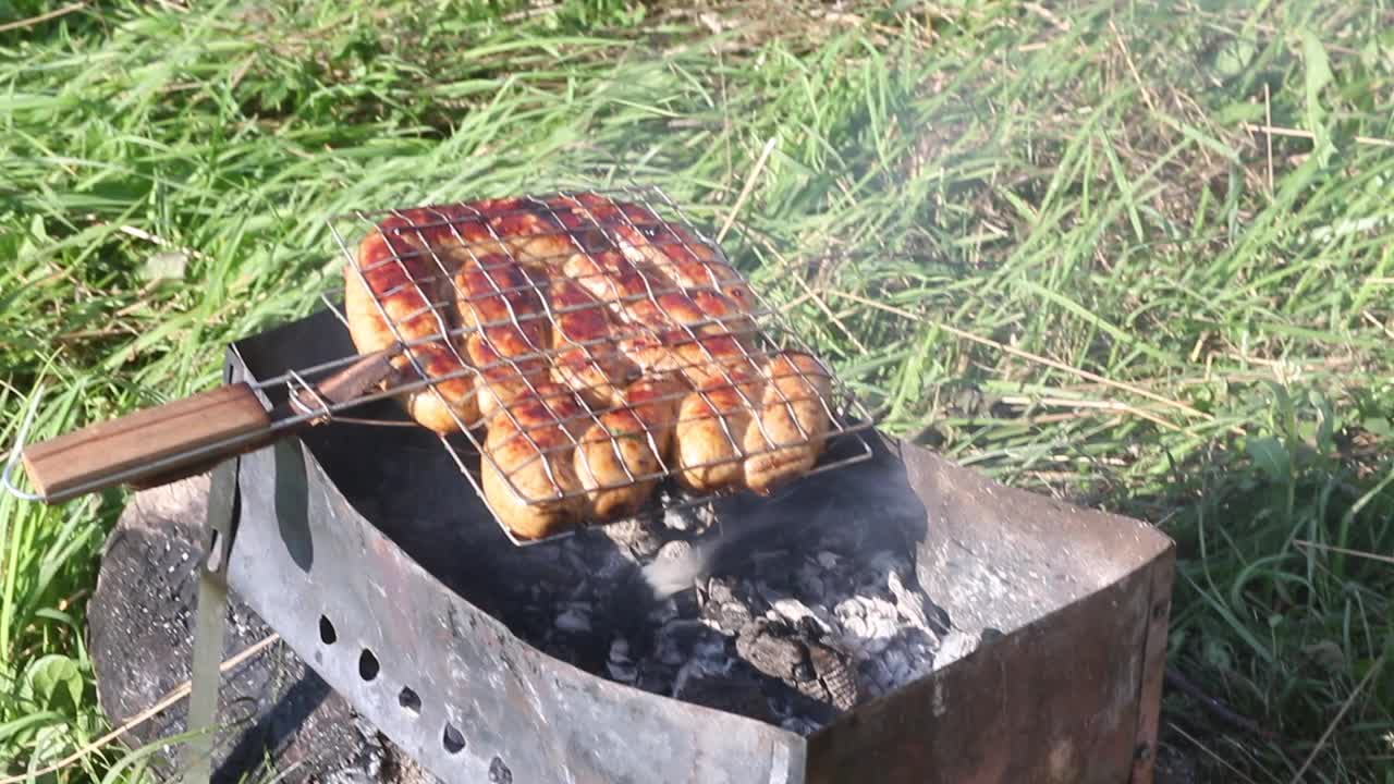 烤架烤香肠。在炭火上烤。在绿草如茵的草地上野餐。特写镜头。视频素材