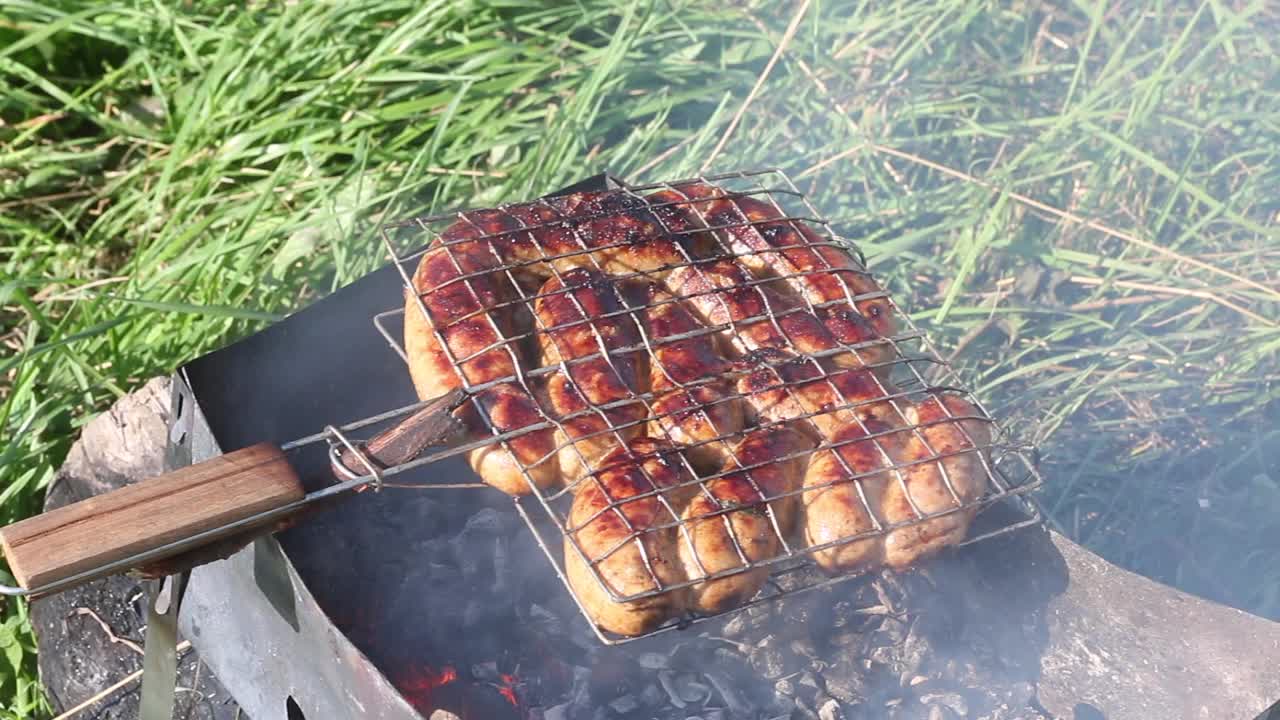 烤架烤香肠。在木炭烤架上。在绿草如茵的草地上野餐。特写镜头。视频素材