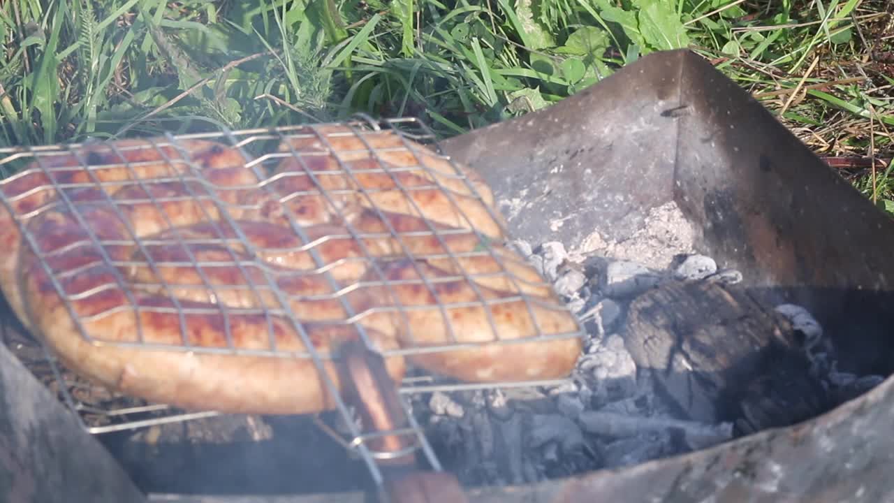 烧烤架与棕色香肠。躺在烤架上，还有余烬。在绿草如茵的草地上。野餐。特写镜头。视频素材