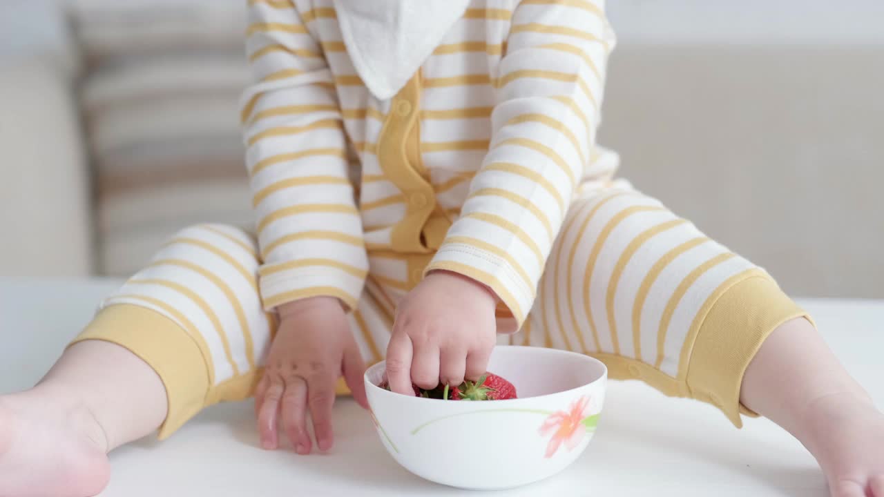 在家吃宝宝的照片。健康食品，午餐时间。孩子做鬼脸。孩子坐在桌子上，手里拿着碗视频素材