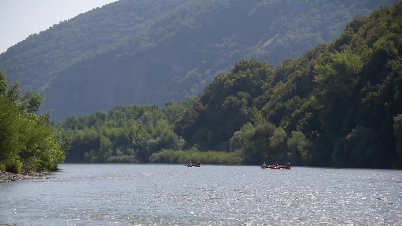 远处有一群人乘着双体船漂浮在山间的河流上视频素材