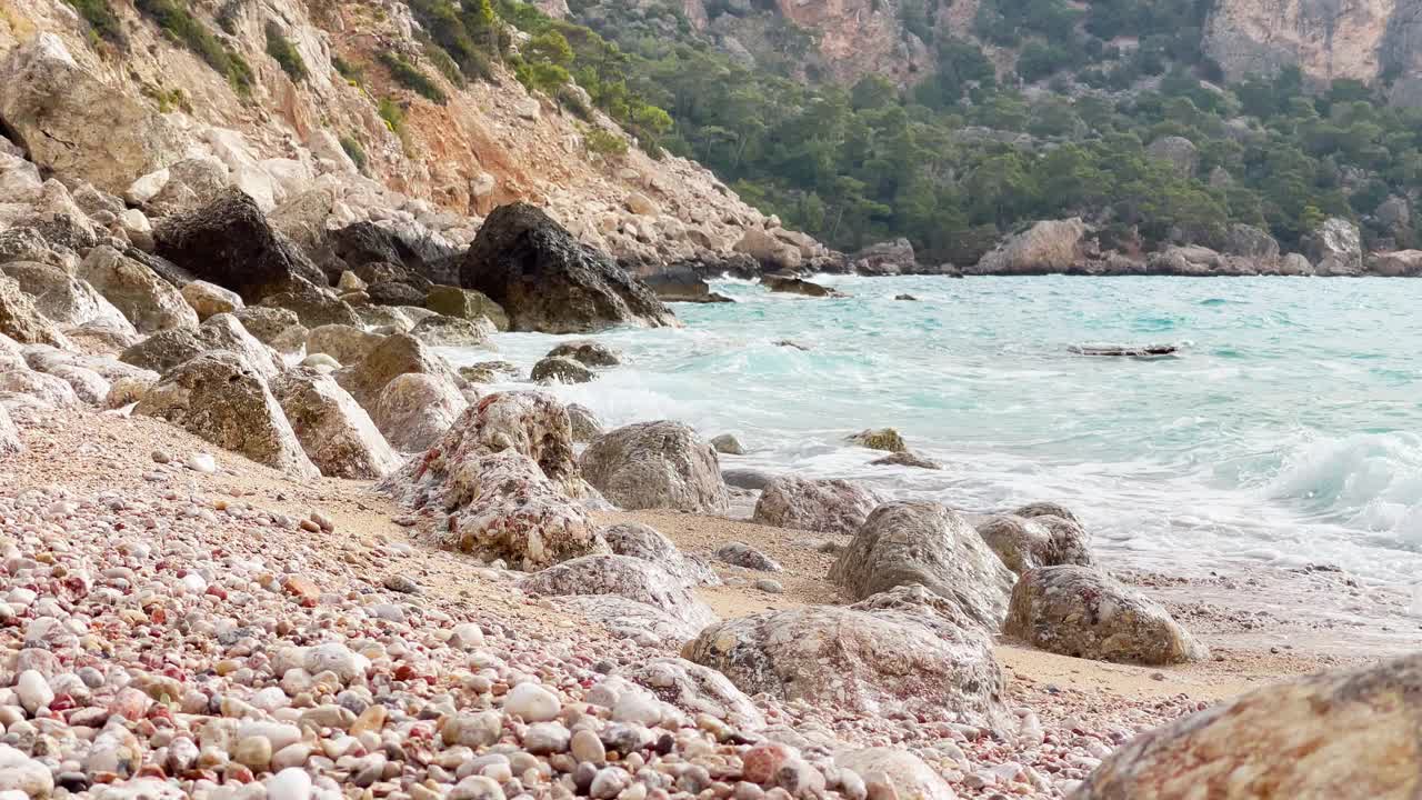 4K慢镜头，海浪翻滚着海岸上的石头，背景是多山的景观。景观、海洋、储水的概念。视频素材