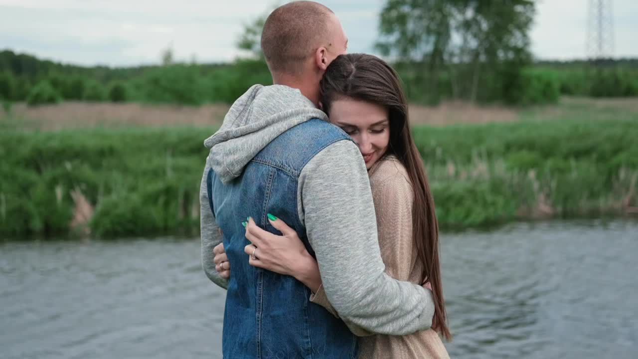 幸福的年轻夫妇在湖边和绿草地的户外。秃头男人和黑发女人。丈夫和妻子。千禧一代。成功的婚姻。真爱视频素材