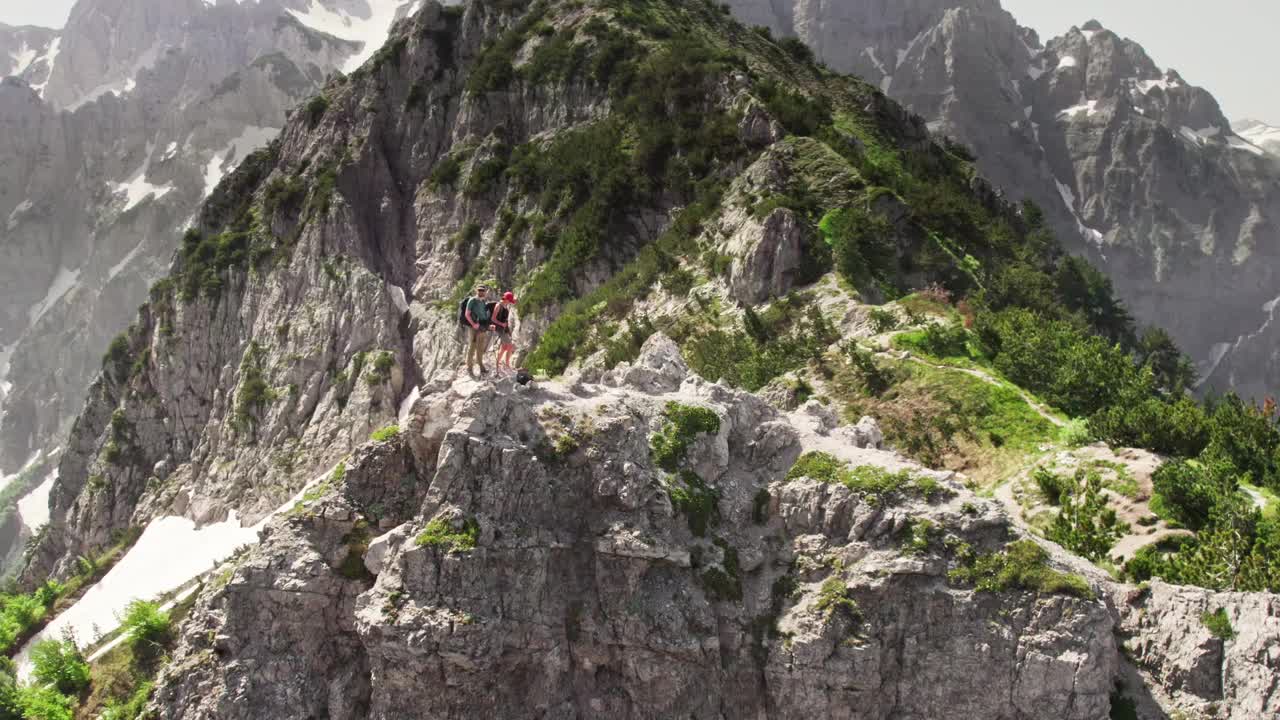 一对夫妇爬到悬崖顶上。两个背包旅行者在高山中飞行。背景是落基山脉和山谷。空中无人机拍摄的视频素材