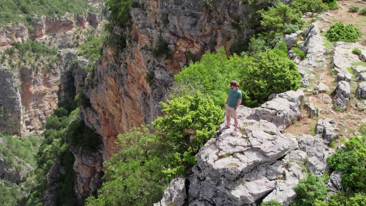 一个人站在悬崖边环顾四周。在峡谷深处的岩石上飞行。成功，目标成就理念。空中无人机拍摄的视频素材