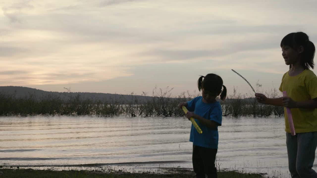 日落时分，亚洲两个孩子在湖边玩泡泡视频素材