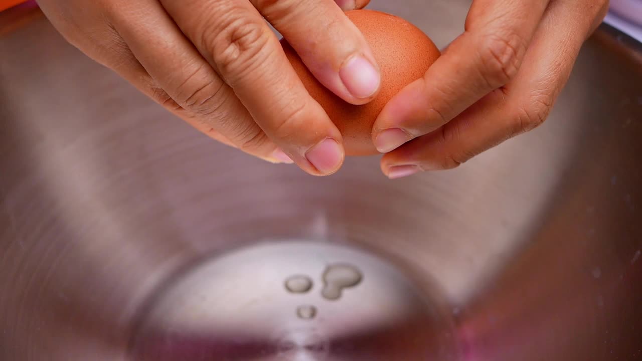 女性的手正在将一个鸡蛋敲进一个不锈钢容器。循序渐进的健康膳食食谱。视频素材