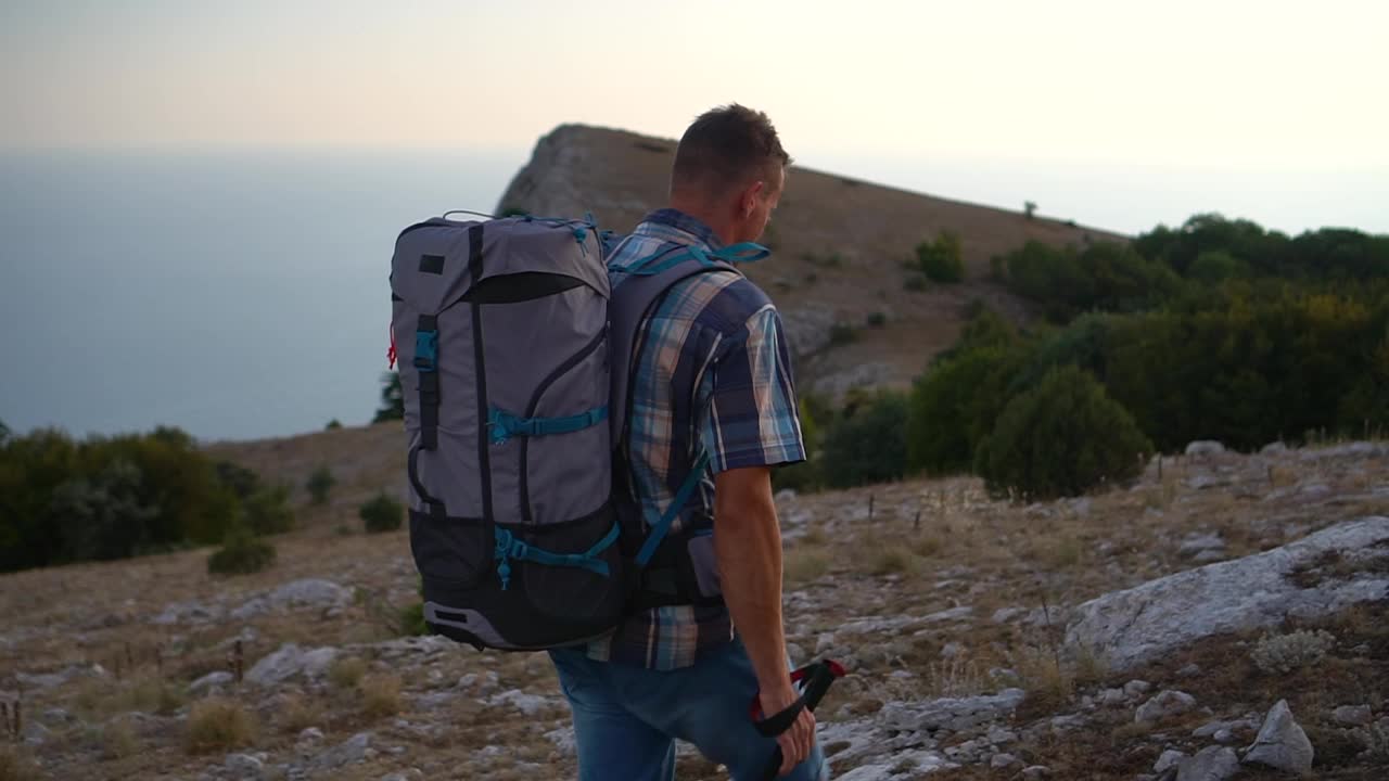 男子徒步旅行在山上徒步旅行岩石草地在晚上Spbd。使用旅游装备，背双肩包和登山杆视频素材