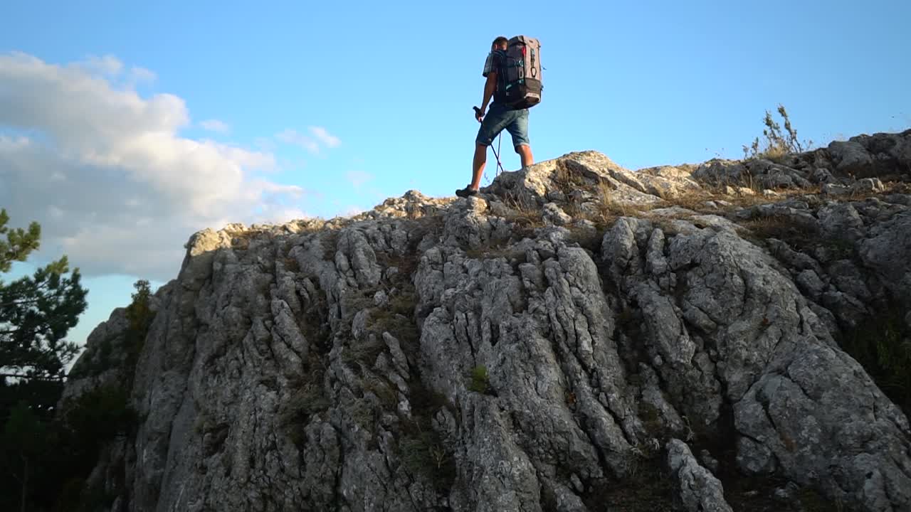 一个年轻的男运动员正在蓝天下的岩石山上徒步旅行视频素材