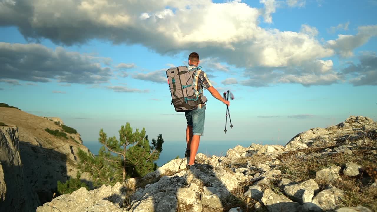 男徒步者背着背包和登山杖，爬上徒步旅行的山顶并举起手。Spbd男人视频素材