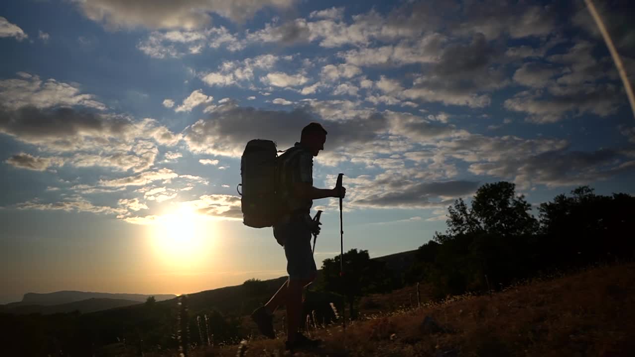 旅行，登山，徒步旅行，男人的剪影，徒步旅行，爬山，在夕阳的光线下爬山。男徒步者步行与徒步视频素材