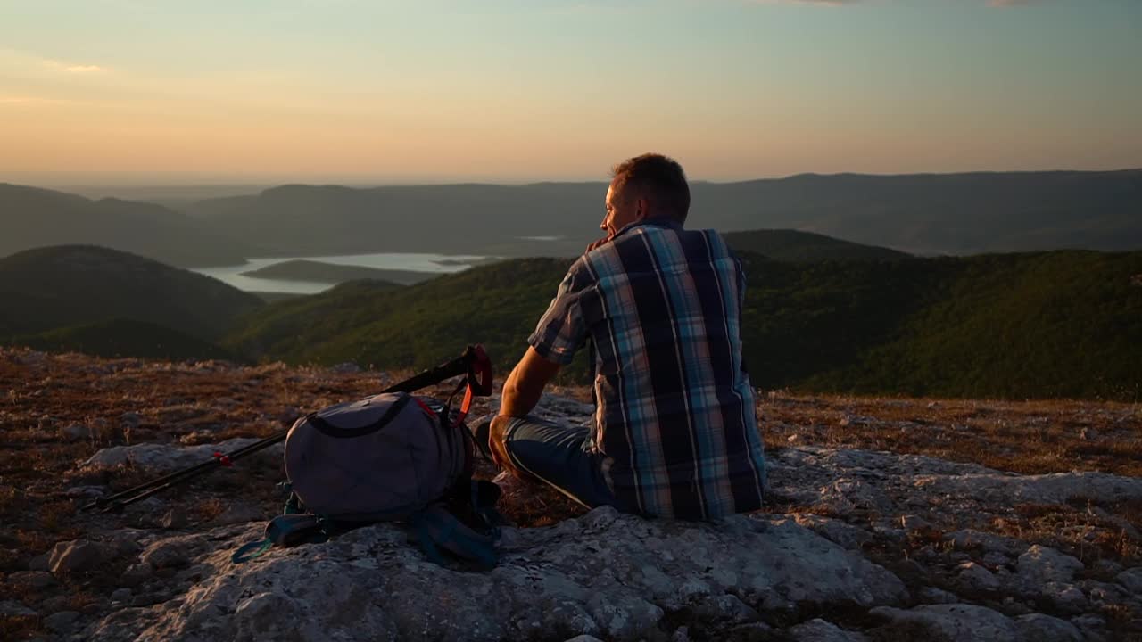 成年男子休息，坐在登山旅行岩石上，欣赏日落美景。男性的徒步旅行者放松。Spbd冥想旅游视频素材