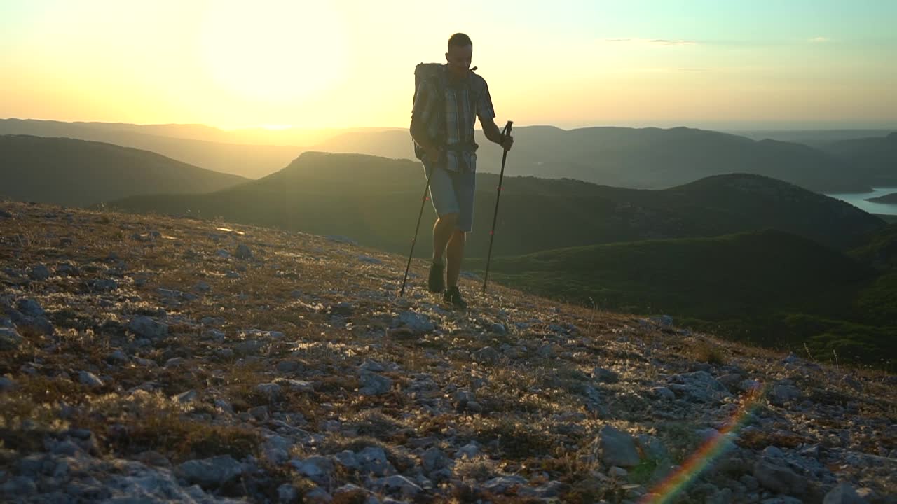 男子游客拄着登山杖在山上徒步旅行山顶在日落时分。夏日远足，男性登山视频素材