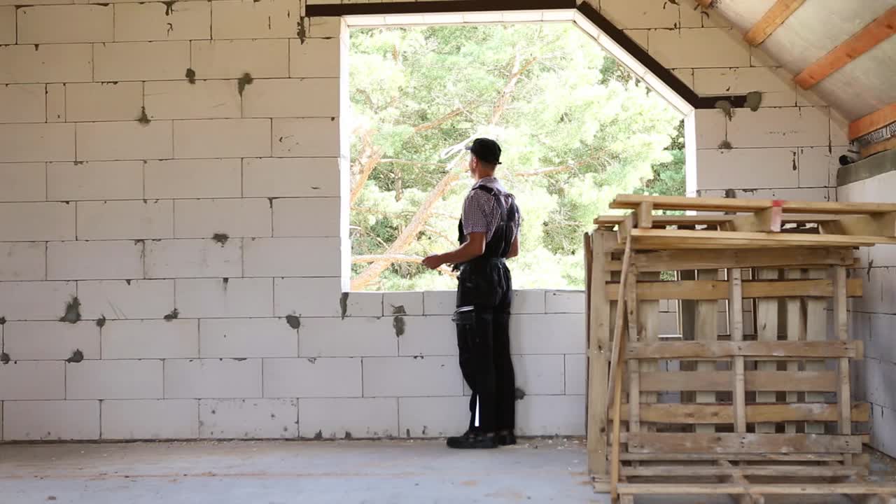 建筑工人们正在用卷尺测量窗洞和砖墙的长度。小屋由多孔混凝土砌块、防护服——连身衣和背心组成视频素材