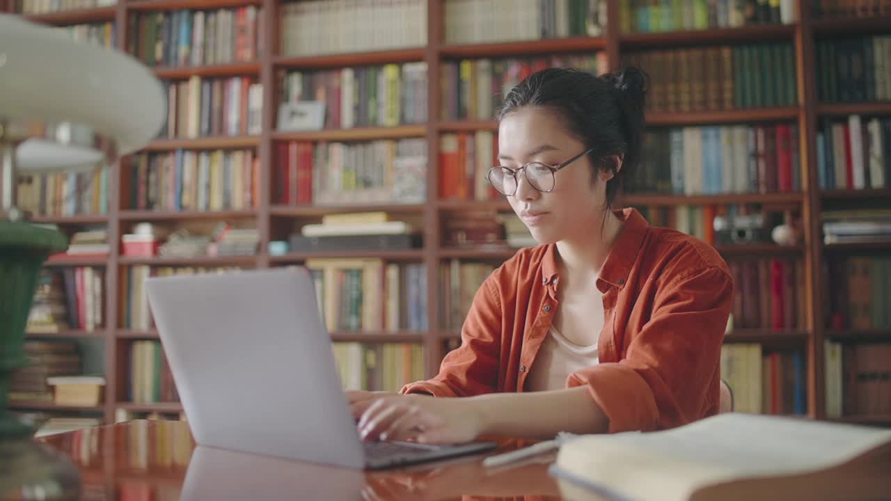 快乐的亚洲女学生完成项目，关闭电脑在大学图书馆视频素材