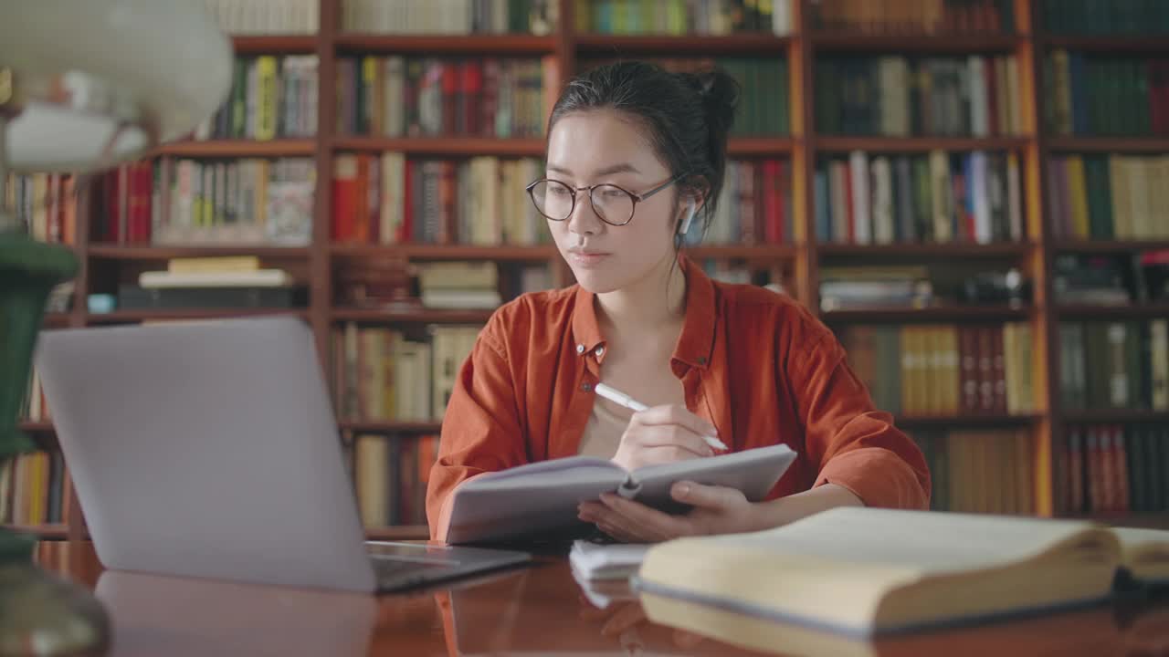 集中的亚洲学生记笔记，在图书馆上在线课程视频素材