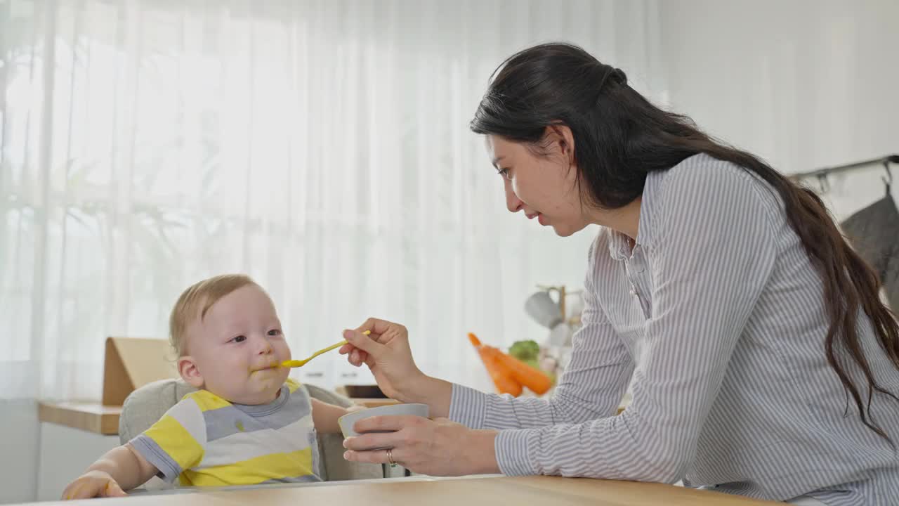 白种人漂亮的妈妈在厨房照顾小男孩。幸福的家庭，可爱的妈妈坐在椅子上为孩子做健康的食物。视频素材