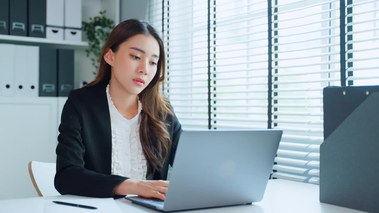 疲惫迷人的亚洲女商人在工作桌上看着许多文件工作。忙碌的女员工由于工作到很晚，在办公室的电脑桌上放着工作文件，感到疲惫头痛视频素材