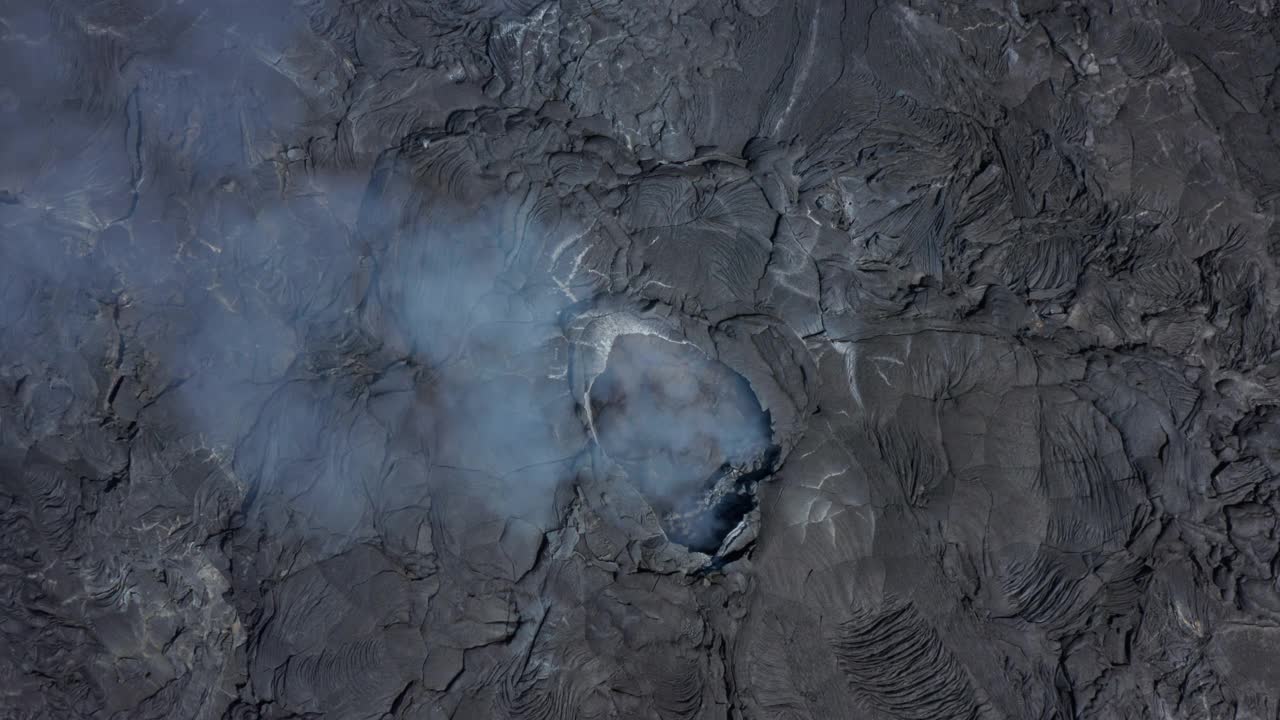 空中鸟瞰从上往下俯瞰法格拉达斯火山冒烟的火山口裂缝洞，无人机上升揭示黑色的熔岩景观，冰岛，白天视频素材