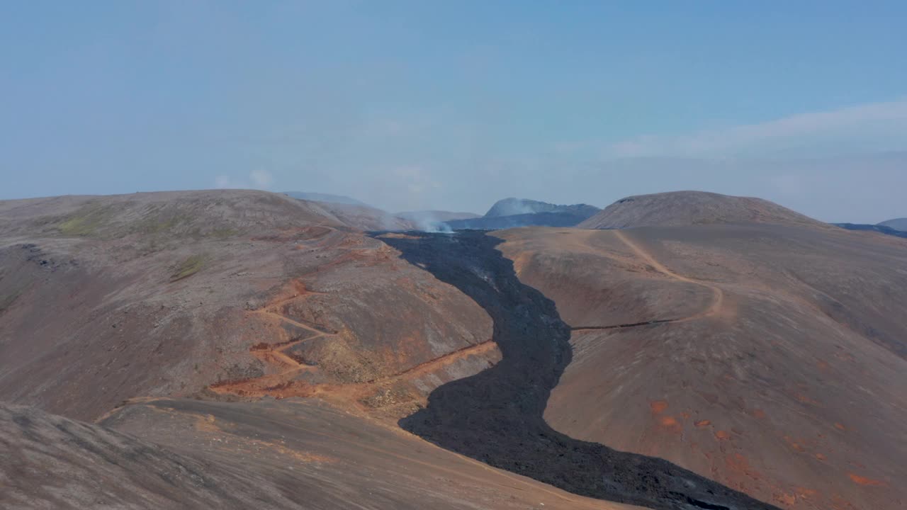 在冰岛fagradalsjall山脉间流动的黑色熔岩河上空盘旋视频素材