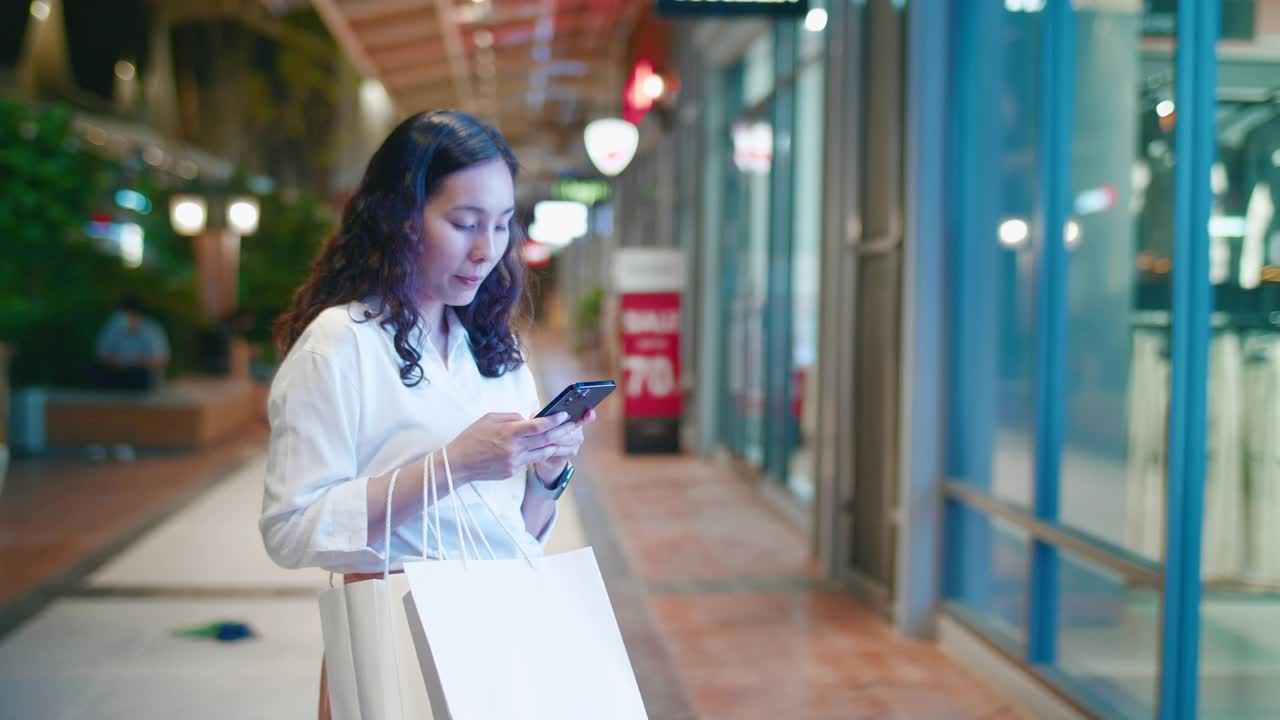 年轻的亚洲女人用电话看着商店的橱窗视频素材