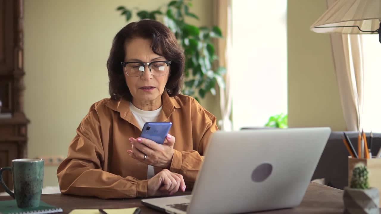 女人在公寓房间的桌子上讲电话和使用笔记本电脑视频素材