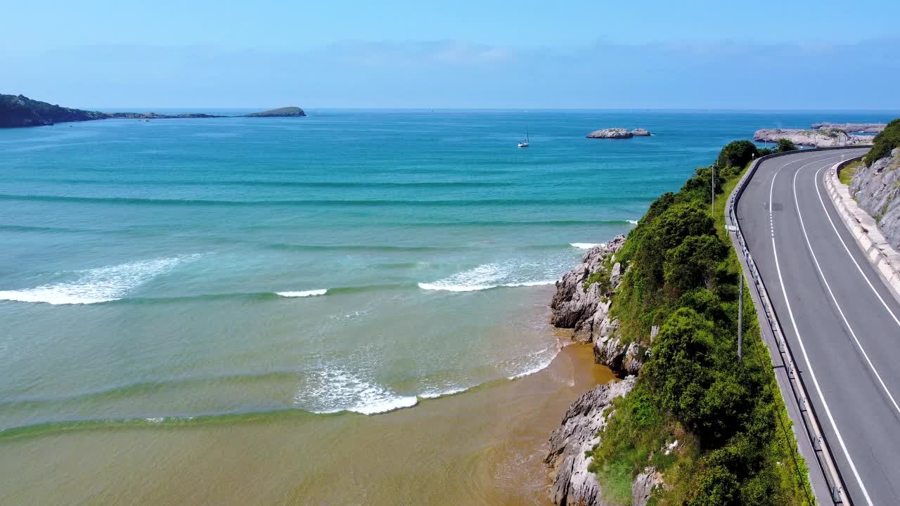 当车辆经过时，无人机在道路上方飞行。在西班牙坎塔布里亚的Oriñón海滩上视频素材