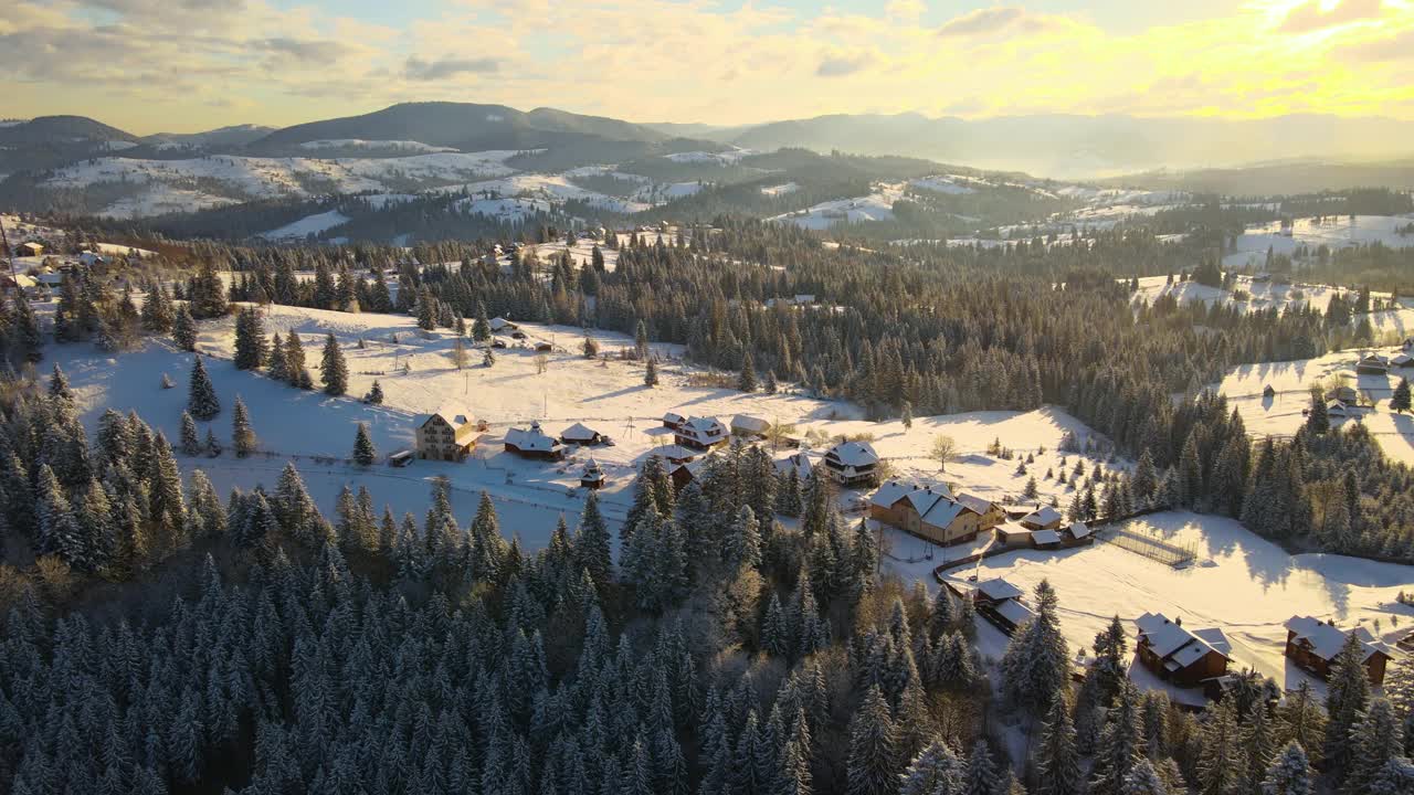 空中冬季景观与小村庄房屋之间的雪覆盖森林在寒冷的山在晚上。视频素材