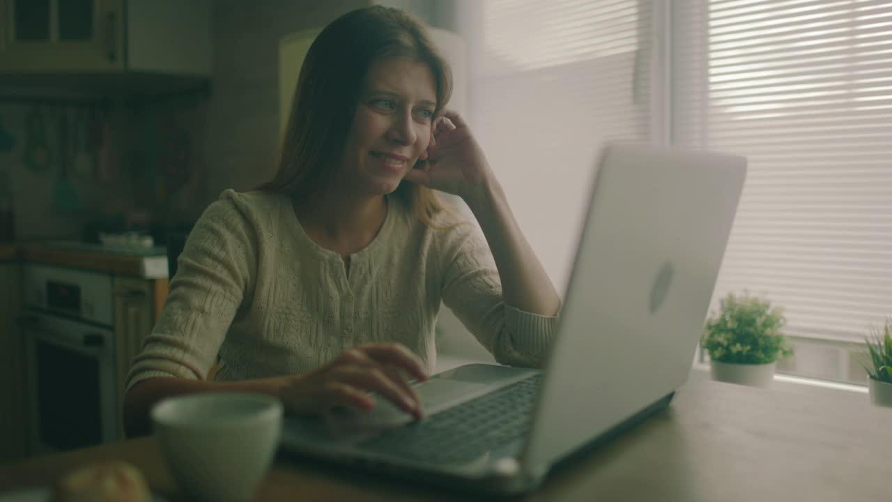 一个女人坐在家里一个大窗户旁边的桌子旁视频素材