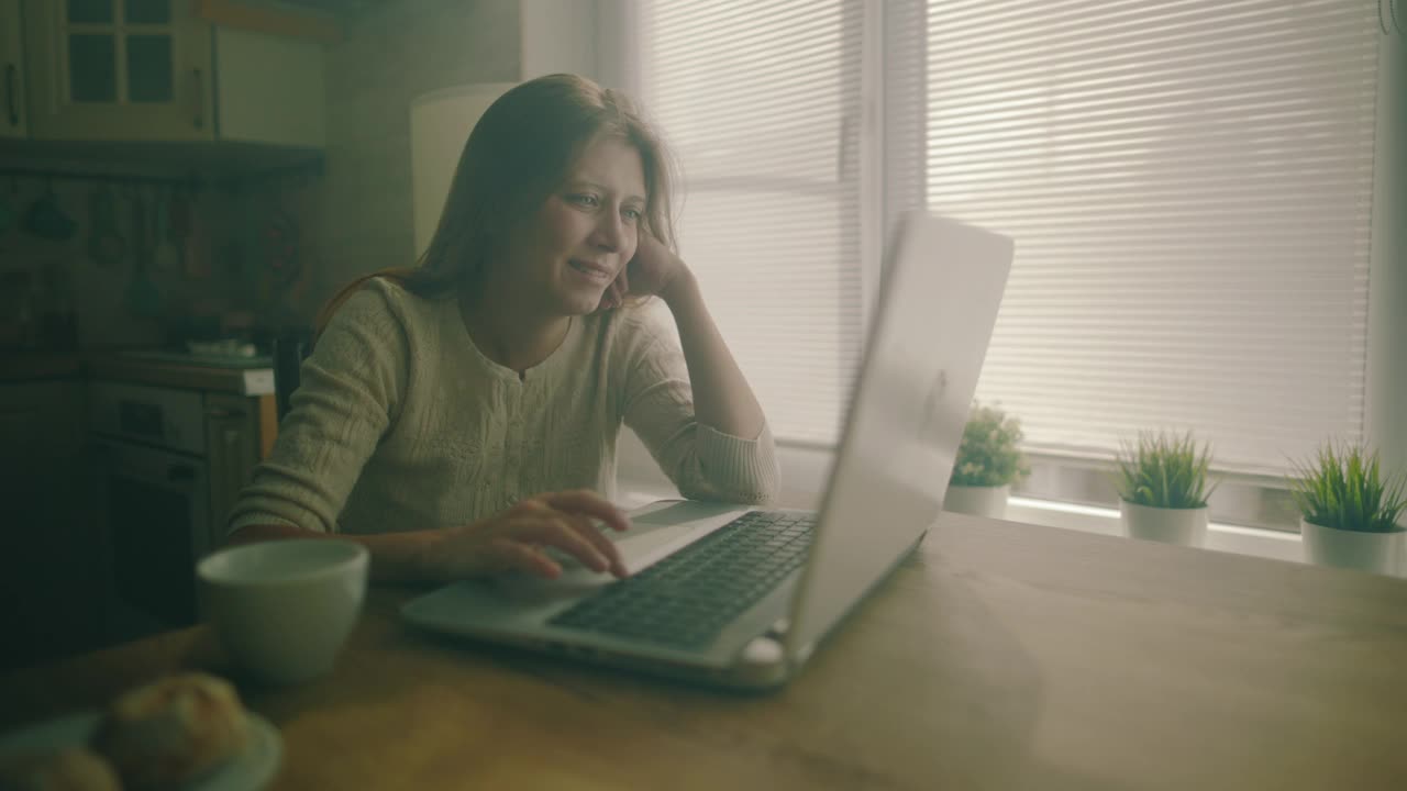 一个女人坐在家里一个大窗户旁边的桌子旁视频素材