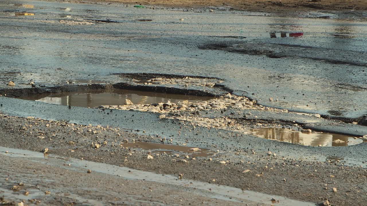 沥青路坑洼，雨后道路基础设施受损。视频素材