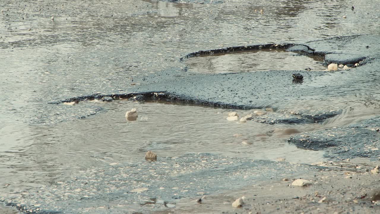 沥青路面上坑坑洼洼，雨后道路基础设施受损。视频素材