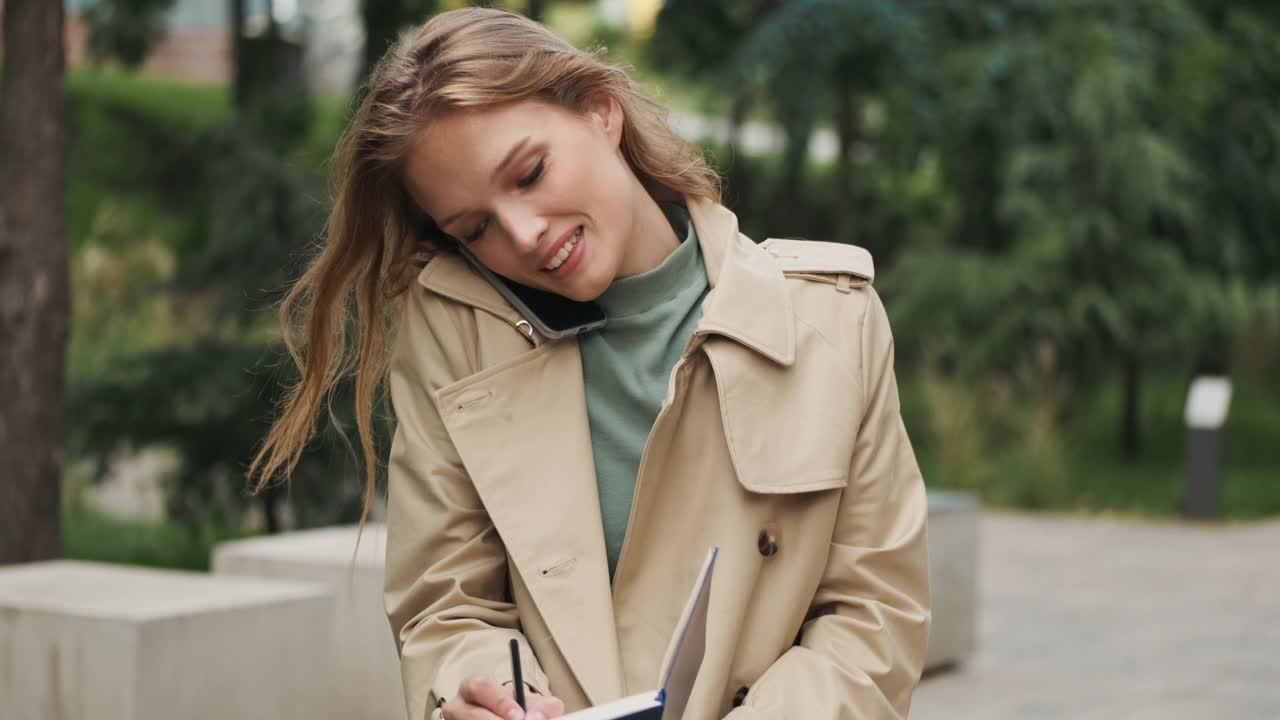 跟踪拍摄的美丽的金发学生女孩打电话与朋友在公园读书视频素材