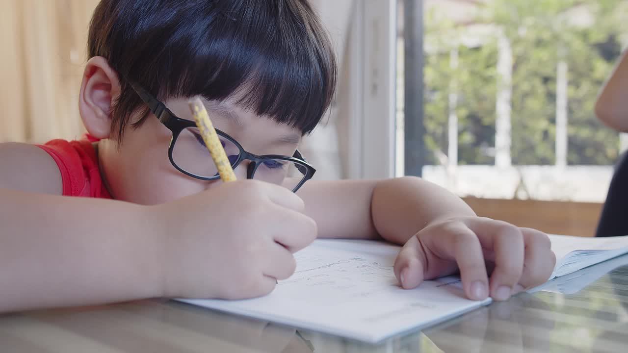 可爱伶俐的小亚细亚小男孩在家里坐在书桌前学习，学生在作业本上写作业，教育观念视频素材