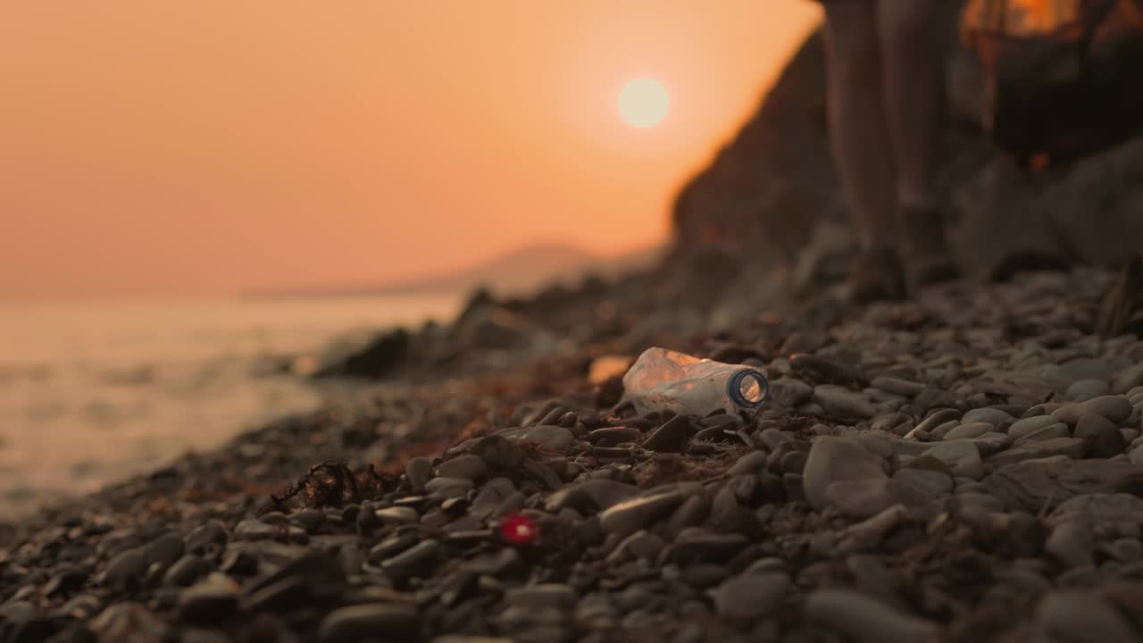 生态的概念。一名戴着橡胶手套的志愿者清理岸边的垃圾。脚的特写。背景是日落。环境保护的概念视频素材