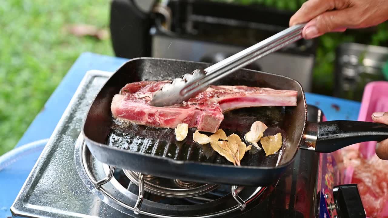 厨师用钳子在平底锅上用大蒜烤牛排丁骨视频素材