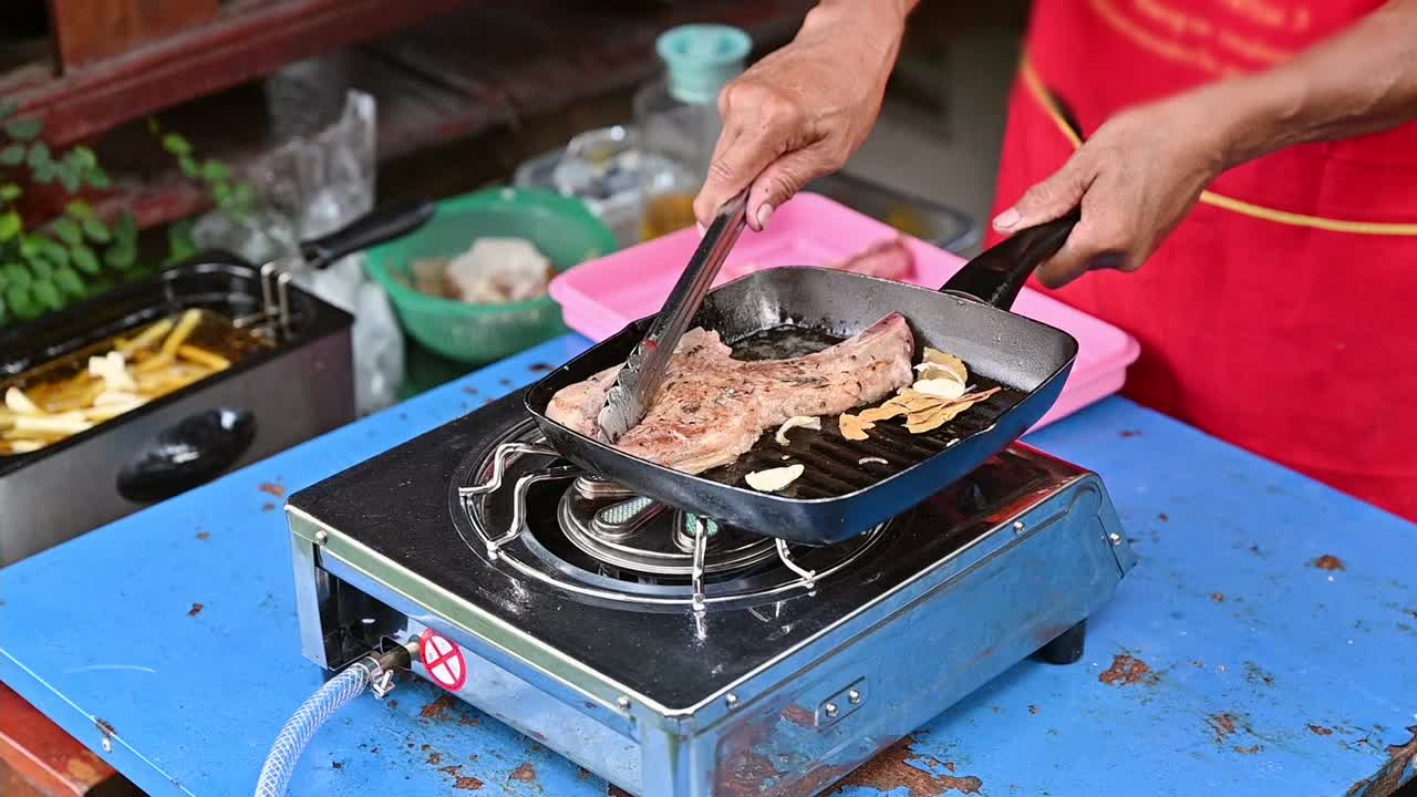 厨师用钳子在平底锅上用大蒜烤牛排丁骨视频素材