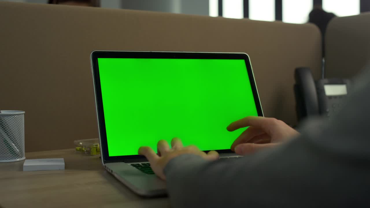 商人在办公室里敲着笔记本电脑的绿色屏幕。人使用笔记本电脑视频素材