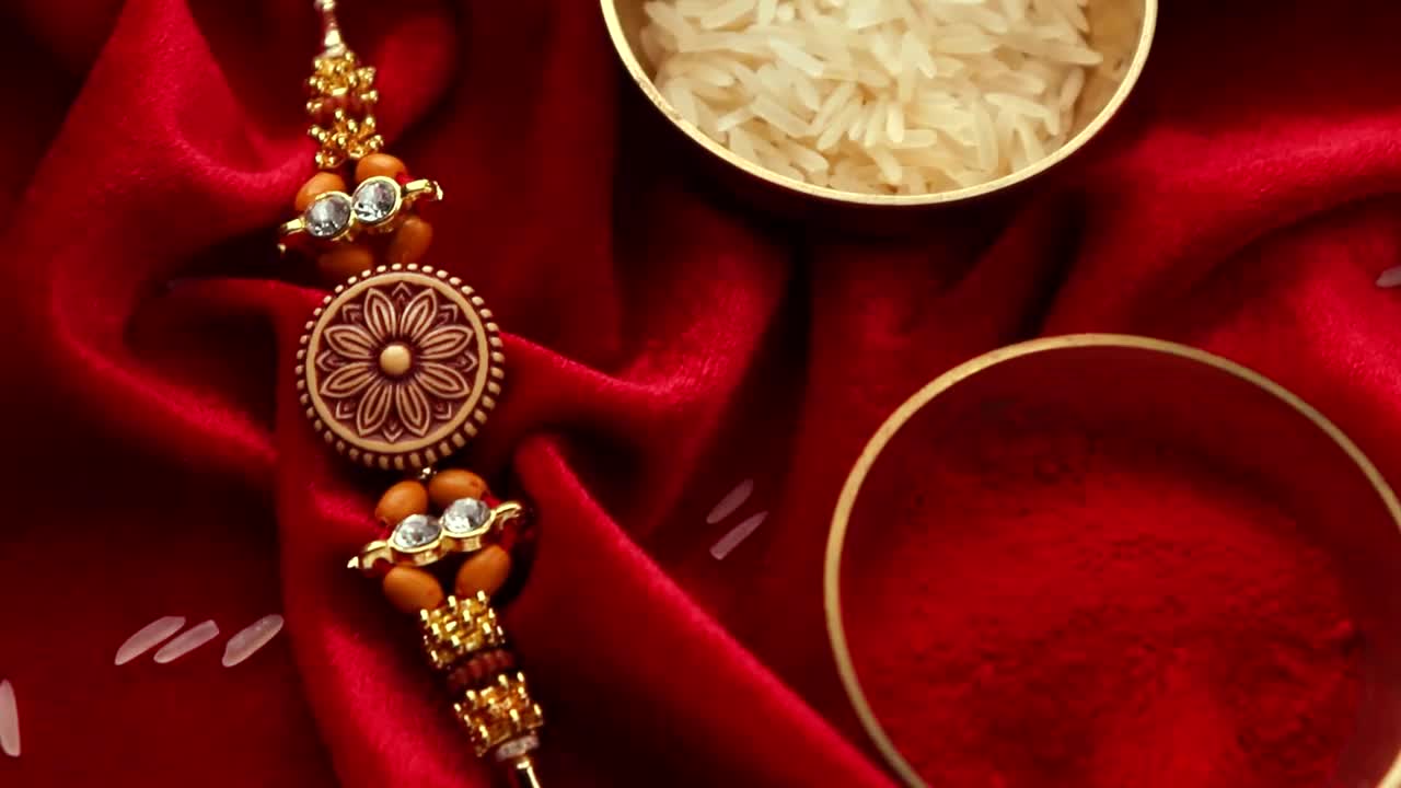 Raksha Bandhan背景以优雅的Rakhi和米粒在红布纹理背景。视频下载