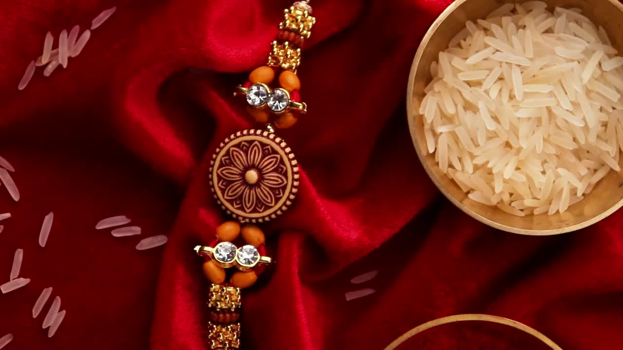 Raksha Bandhan背景以优雅的Rakhi和米粒在红布纹理背景。视频下载