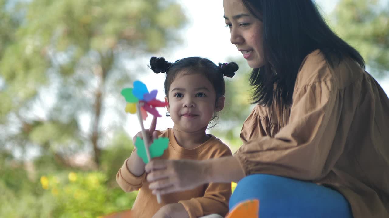 妈妈和小女孩躺在垫子上野餐，在公园里玩风车吹玩具视频素材