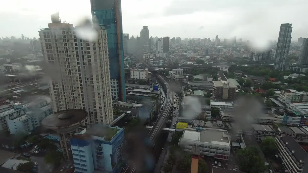 雨点落在窗户上。鸟瞰图。在泰国曼谷的雨季，起居室窗外下着雨。窗外是模糊的雨，城市建筑，道路和天空。视频素材