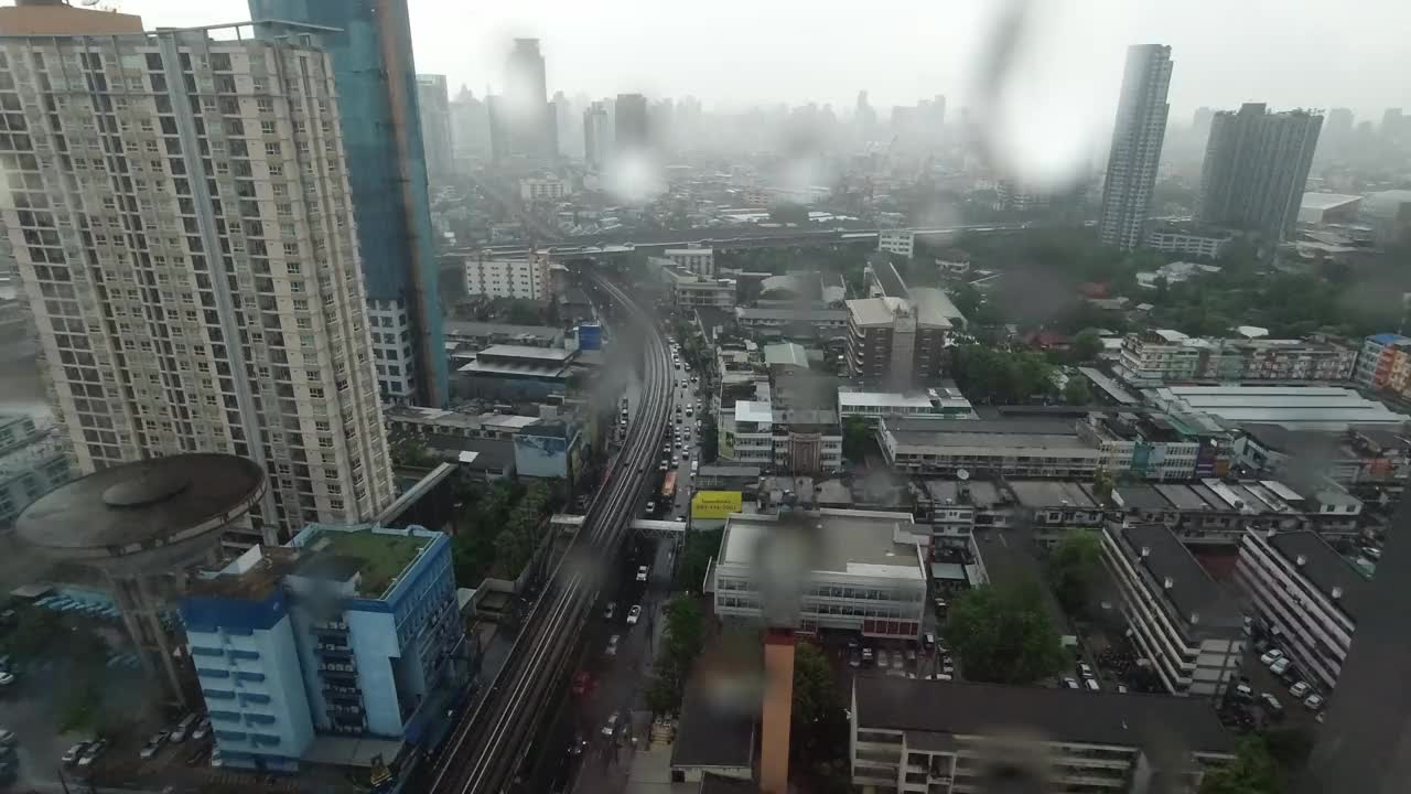 雨点落在窗户上。鸟瞰图。在泰国曼谷的雨季，起居室窗外下着雨。窗外是模糊的雨，城市建筑，道路和天空。视频素材